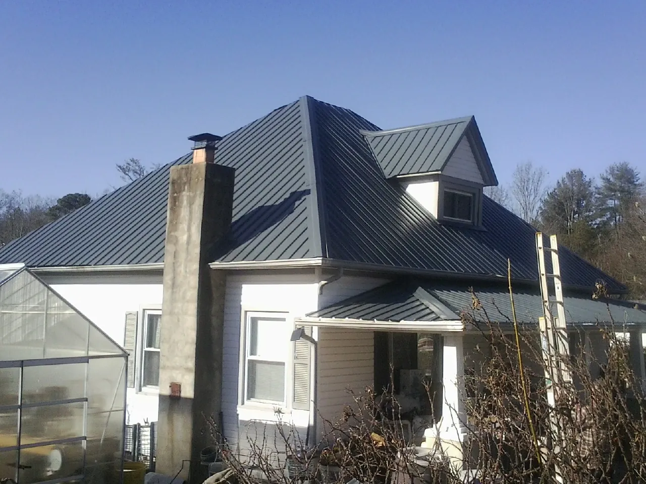 Dark blue standing seam metal roof on a white farmhouse with dormer — Slate & Tile Roof Repair by Roofing Brothers in Baskerville