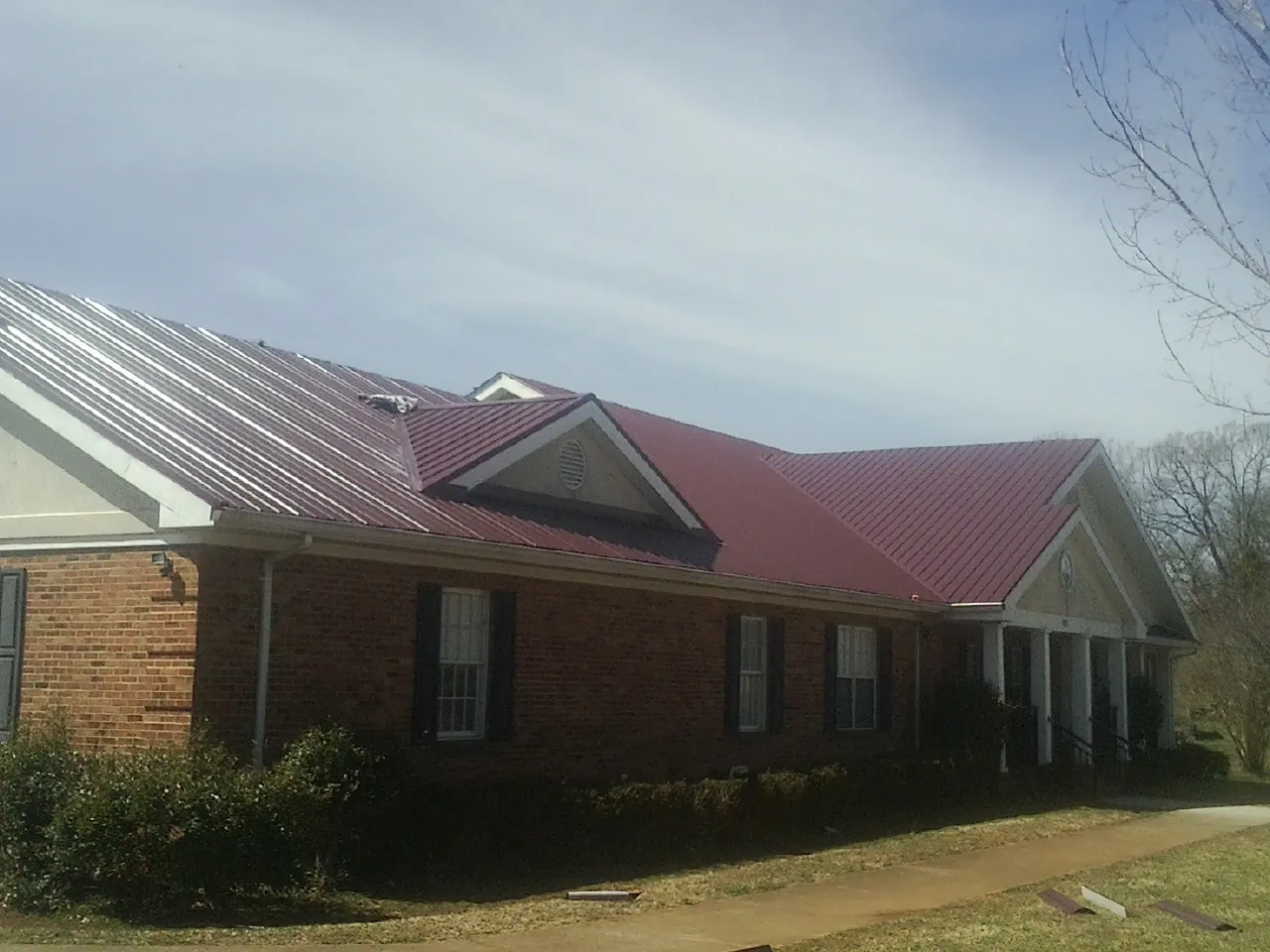 Red metal roof with gabled entries on a long brick building, from a Hail Damage Roof Repair job in Baskerville