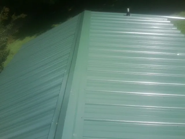 New green metal panels meeting at the ridge of a roof — Flat Roof Repair work by our crew in Baskerville